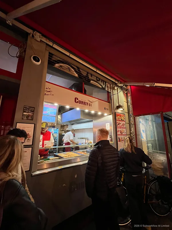 The counter at Curry 61, a currywurst stand, with people queueing at night