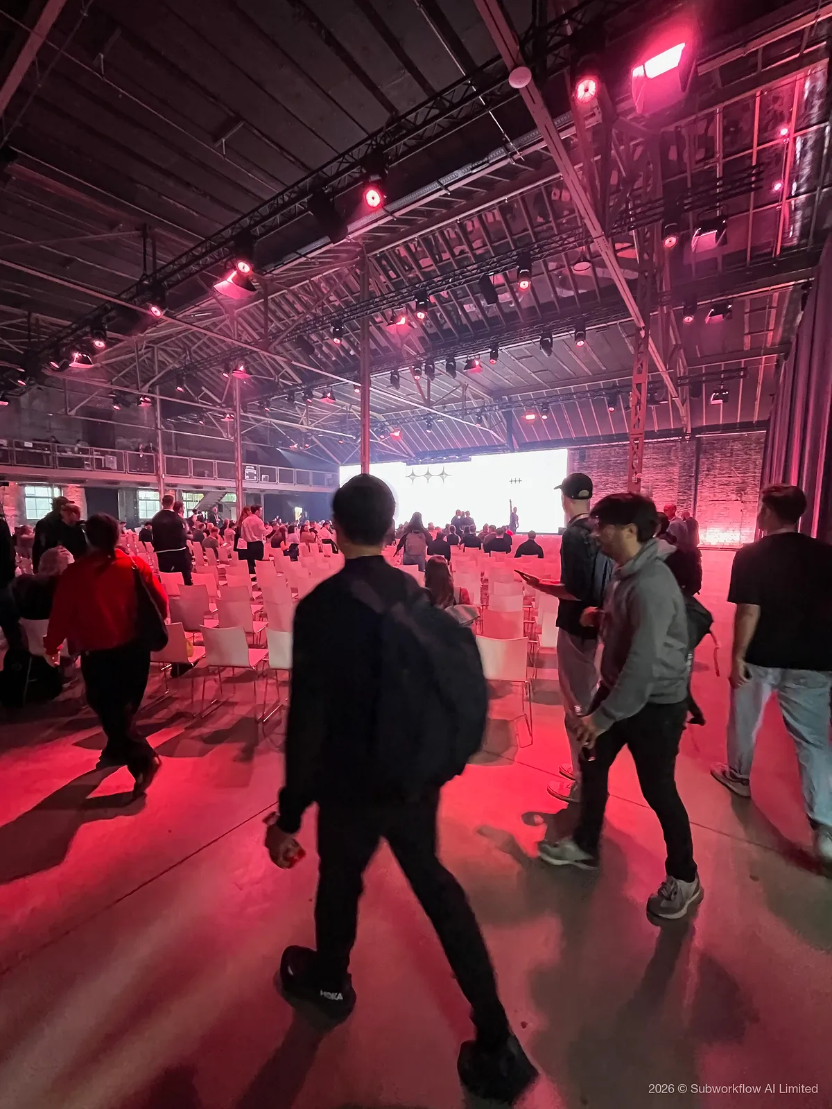 People finding seats in the main hall before a keynote, under pink stage lights