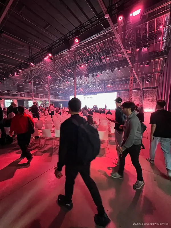 People finding seats in the main hall before a keynote, under pink stage lights