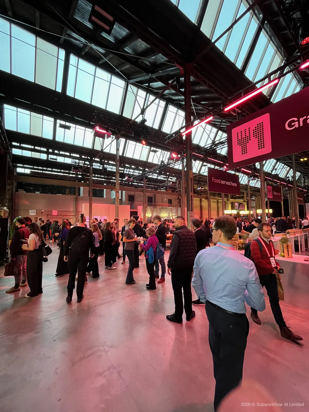 Attendees talking in the glass-roofed hall by the food counters