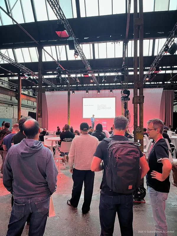 A crowd standing to watch a talk on a side stage