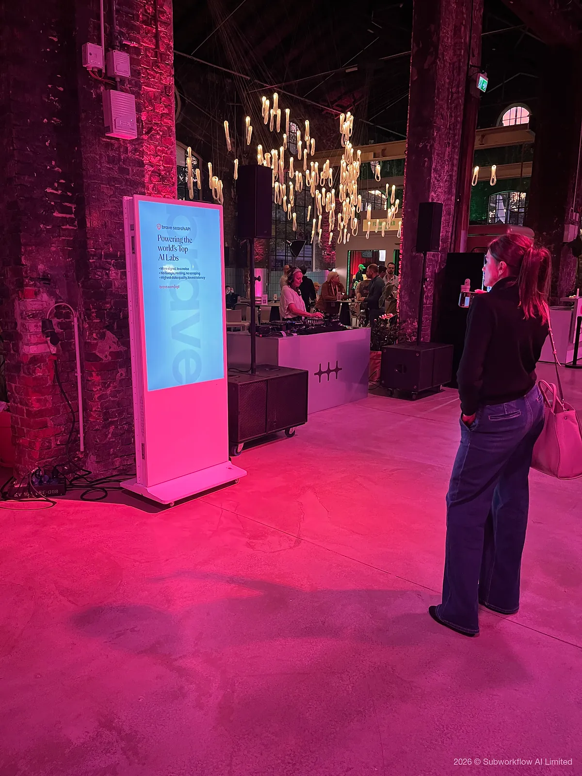 A DJ under hanging neon lights, beside a Brave Search API sign